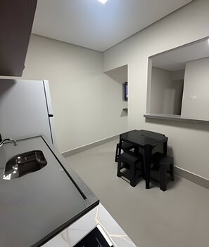 A modern kitchen with a black countertop and a small dining area with a table and stools. - Studios Jocatita (Cuiabá)