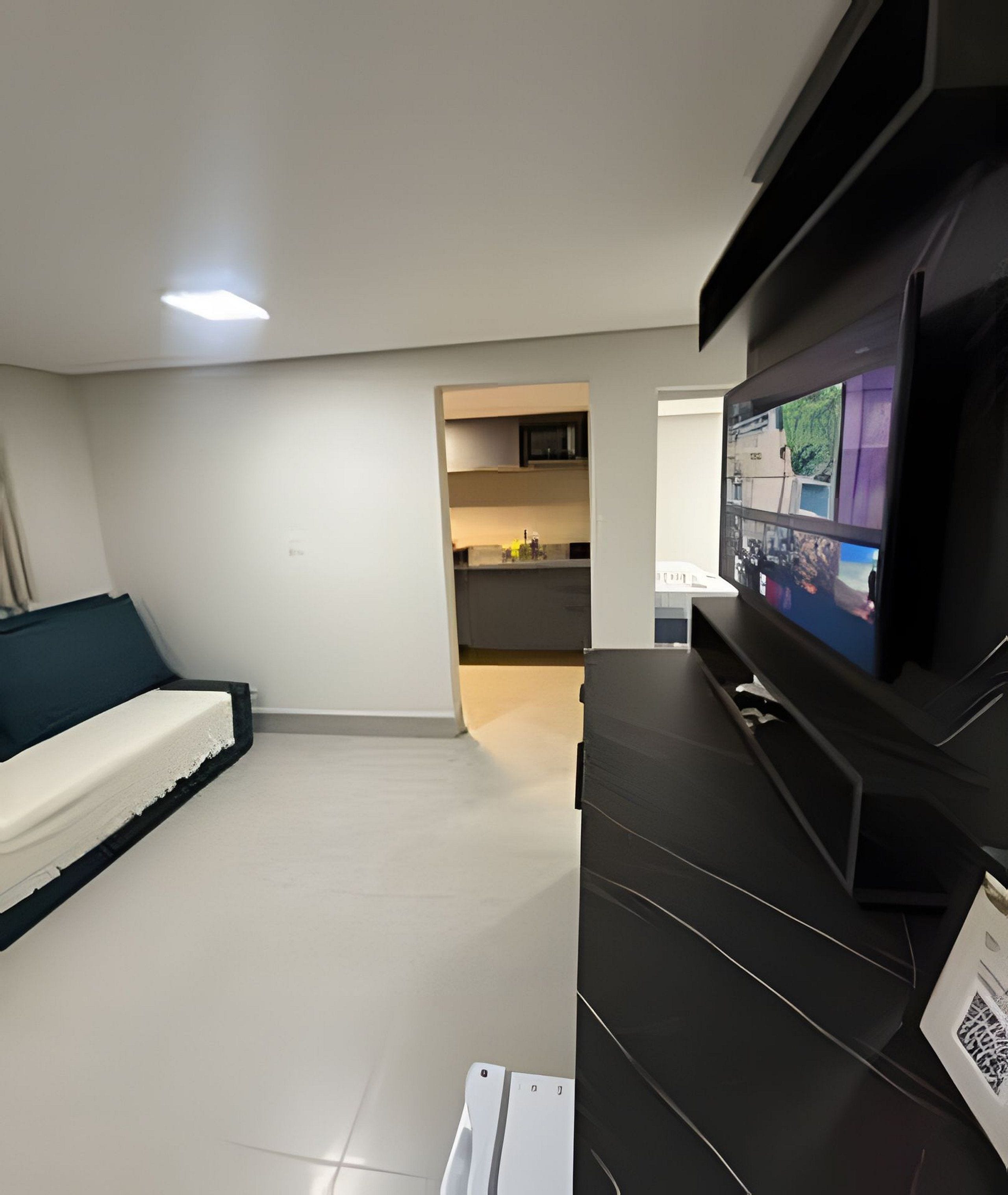 Una sala de estar moderna con una televisión de pantalla plana, un sofá y una zona de cocina al fondo.