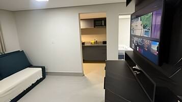 Una sala de estar moderna con una televisión de pantalla plana, un sofá y una zona de cocina al fondo.