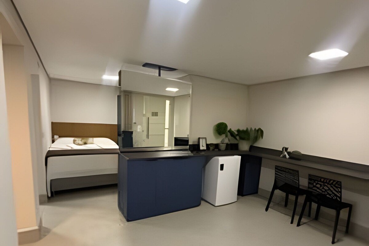 A modern hotel room with a bed, a small desk, a chair, a mirror, and a potted plant.