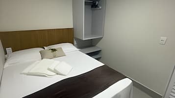 Una habitación de hotel con una cama, una mesita de noche, un armario y un pequeño estante.