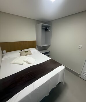 A hotel room with a bed, a bedside table, a wardrobe, and a small shelf. - Studios Jocatita (Cuiabá)