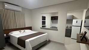 Una habitación de hotel moderna con cama, kitchenette pequeña y ventana con persianas.