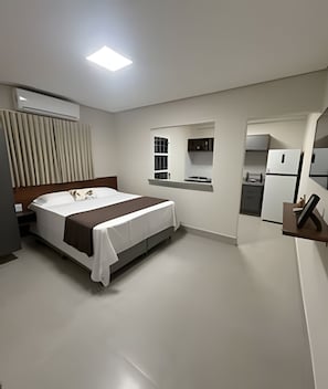 A modern hotel room with a bed, a small kitchenette, and a window with blinds. - Studios Jocatita (Cuiabá)