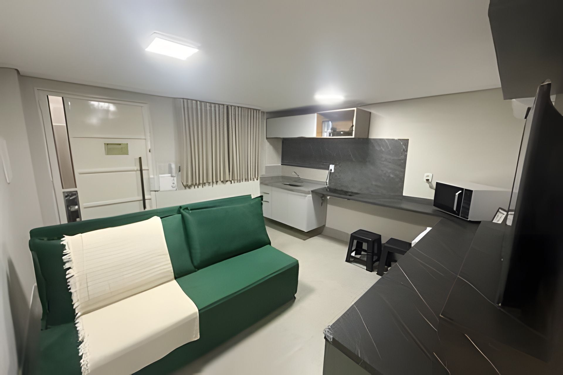 A compact living space with a green sofa, a kitchenette, and a small dining area.