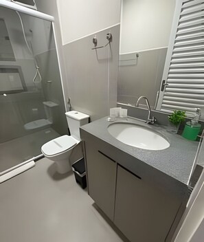 A modern bathroom with a glass-enclosed shower, a white toilet, a sink with a mirror, and a small green plant.