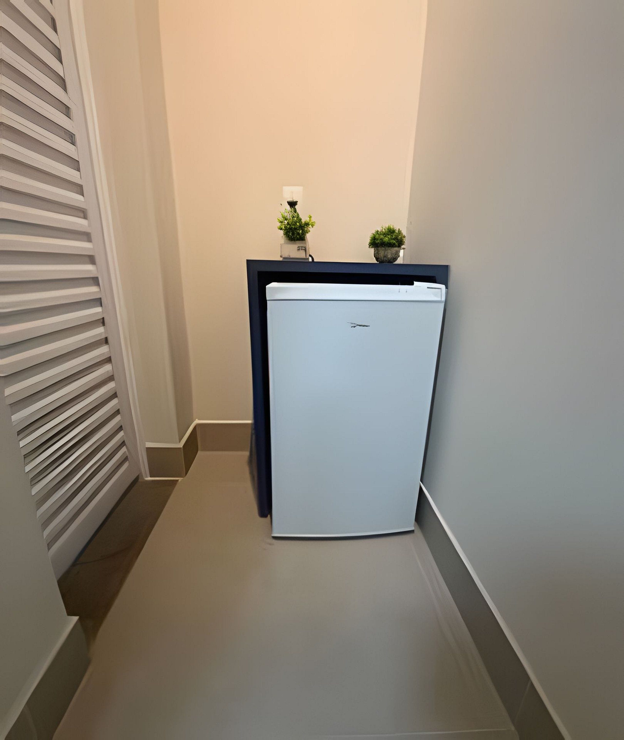 A narrow hallway with a white refrigerator and two potted plants on a counter.
