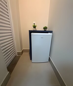 A narrow hallway with a white refrigerator and two potted plants on a counter. - Studios Jocatita (Cuiabá)