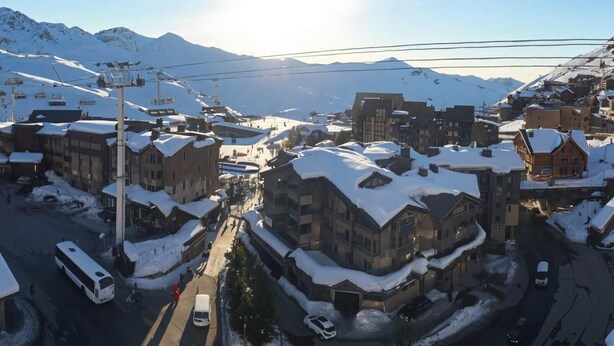 A snow-covered town with buildings, a bus, and a mountain in the background.