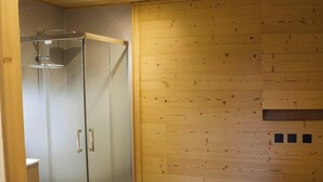 A room with a glass-enclosed shower, wooden walls, and a bed with a white cover.
