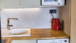 A compact kitchen with a white sink, a red kettle, a microwave, and a Siemens dishwasher.