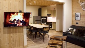 A modern living room with a TV, dining table, chairs, a sofa, and a fireplace.