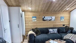 A cozy living room with a wooden ceiling, a sofa set, a coffee table, and two wall-mounted posters.