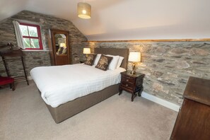 A bedroom with a large bed, stone walls, a wooden dresser, and a mirror.