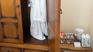 Une armoire en bois avec une penderie, une petite table avec des articles de toilette et un interrupteur sur le mur.