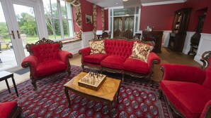 Une pièce avec un canapé rouge, une table basse en bois sur laquelle est posé un jeu d’échecs, et des tapis à motifs.
