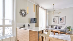A modern kitchen with a central island, a dining area with a sofa and coffee table, and a living room with a TV and artwork.
