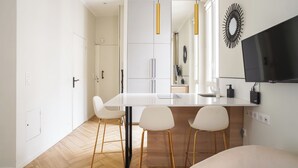 A modern kitchen with white cabinets, a central island with bar stools, pendant lighting, and a flat-screen TV mounted on the wall.