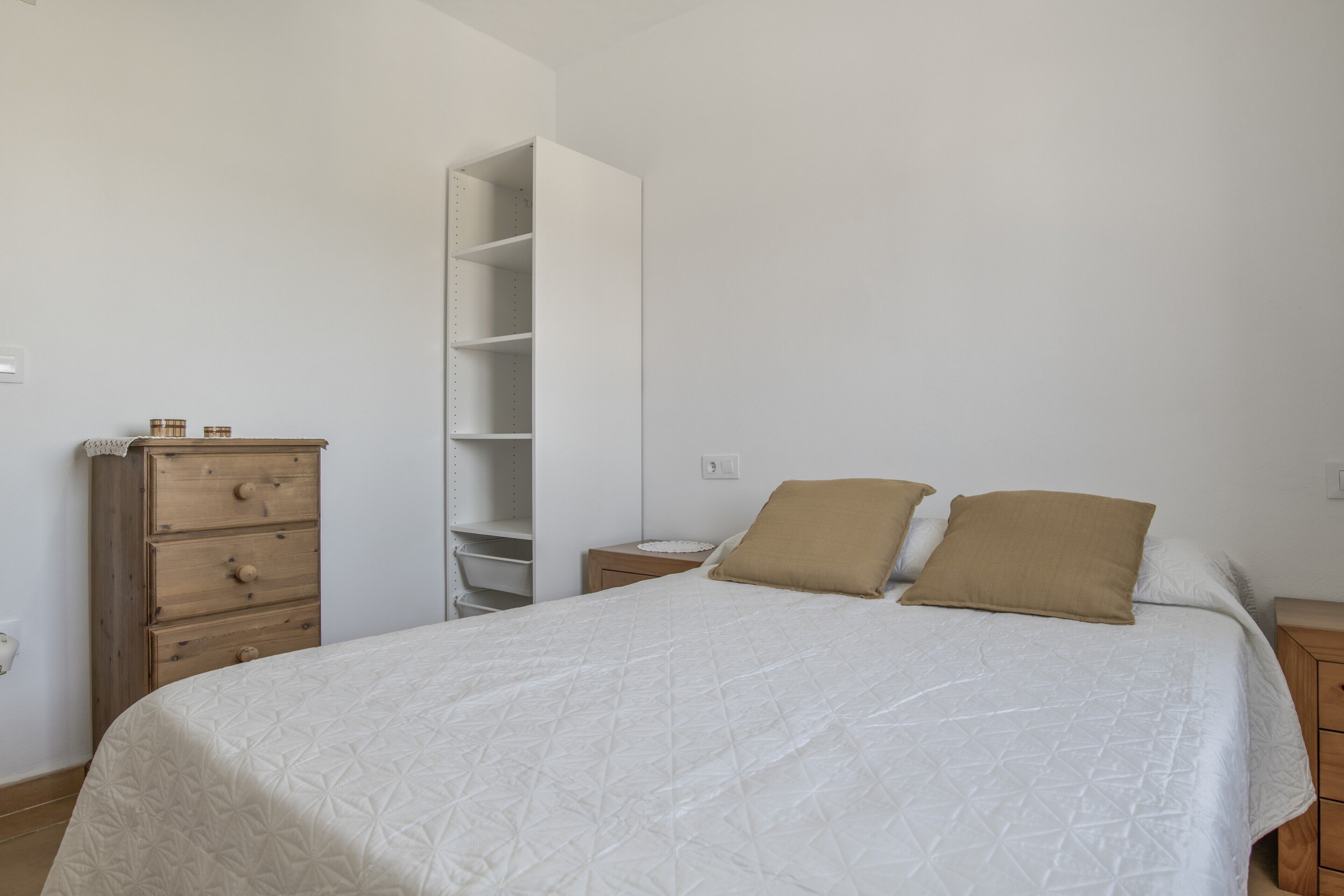 A bedroom with a bed, two pillows, a wooden dresser, and a white wardrobe.