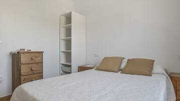 A bedroom with a bed, two pillows, a wooden dresser, and a white wardrobe.