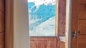 A wooden cabin with a large window, wooden walls, and a view of a mountainous landscape.