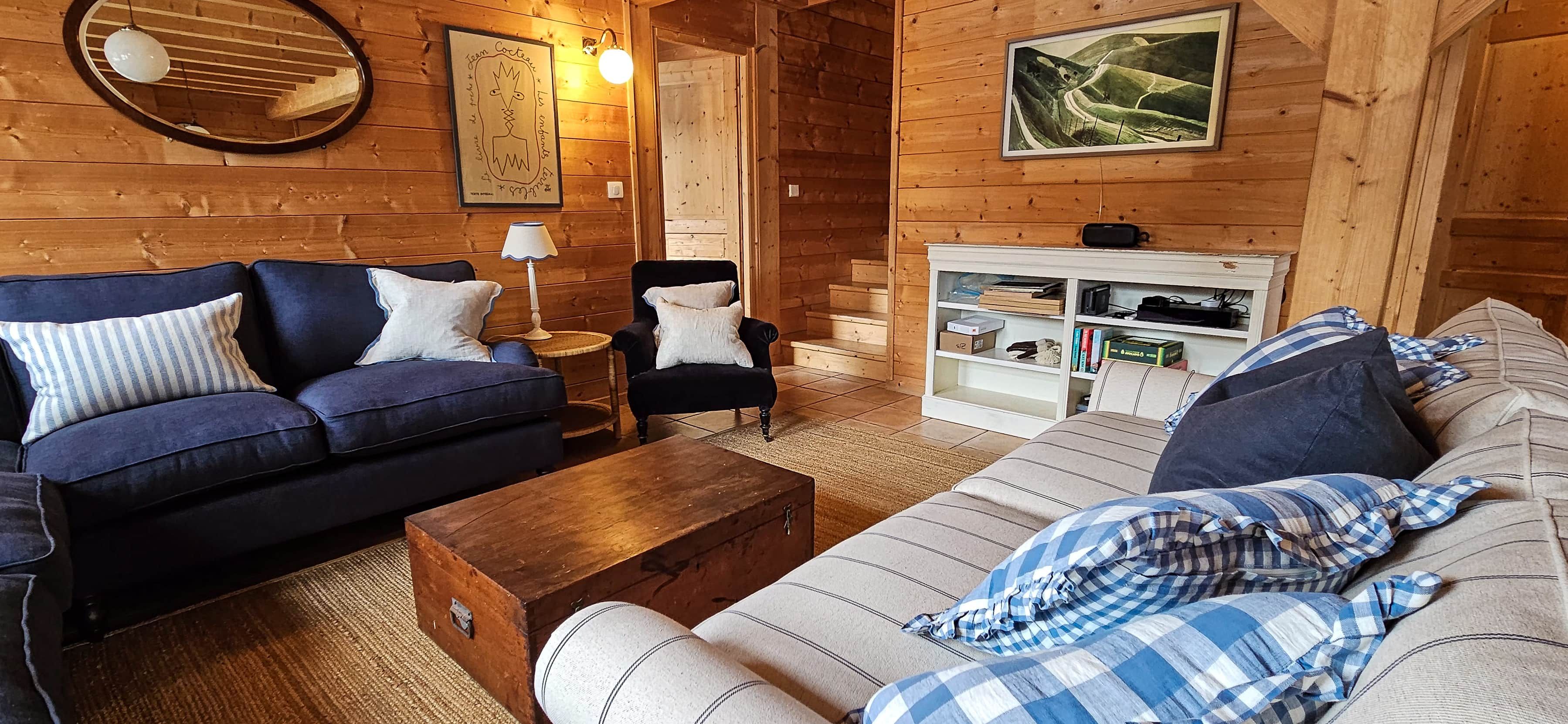 Ein gemütliches Blockhaus-Interieur mit einem blauen Sofa, einem gestreiften Sessel, einem Holztisch und einem Bücherregal.