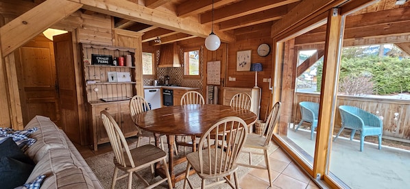A wooden cabin interior with a dining area, kitchen, and a view of the outdoors.