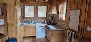 A compact kitchen with wooden cabinets, a dishwasher, a stove, and a window with a view of the outdoors.