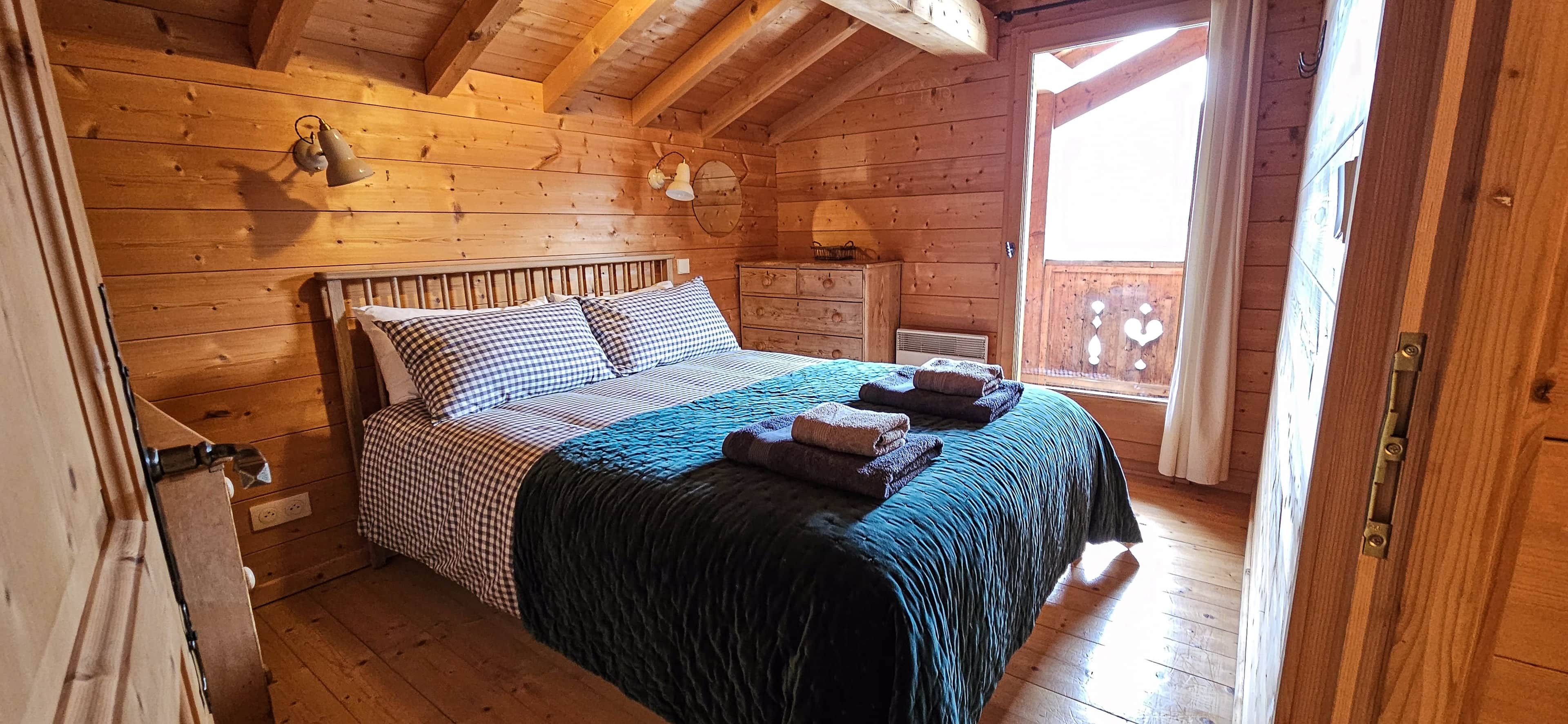 A wooden cabin bedroom with a bed, pillows, a nightstand, and a window.