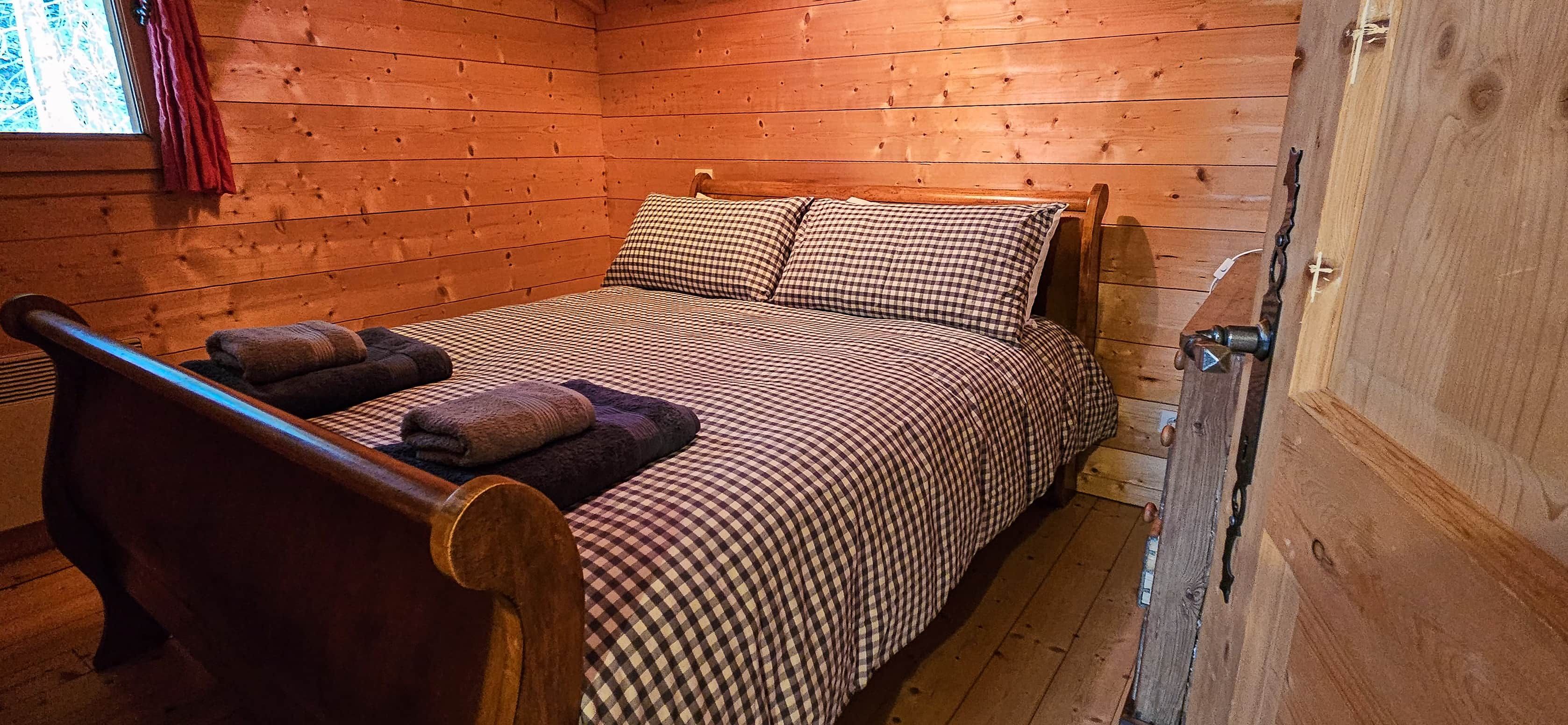 Une pièce de cabane en bois comprenant un lit, une chaise et une fenêtre avec des rideaux.