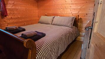 Une pièce de cabane en bois comprenant un lit, une chaise et une fenêtre avec des rideaux.