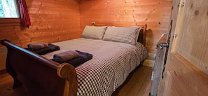 A wooden cabin room with a bed, a chair, and a window with curtains.