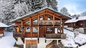 A wooden chalet with a balcony, surrounded by snow-covered trees.