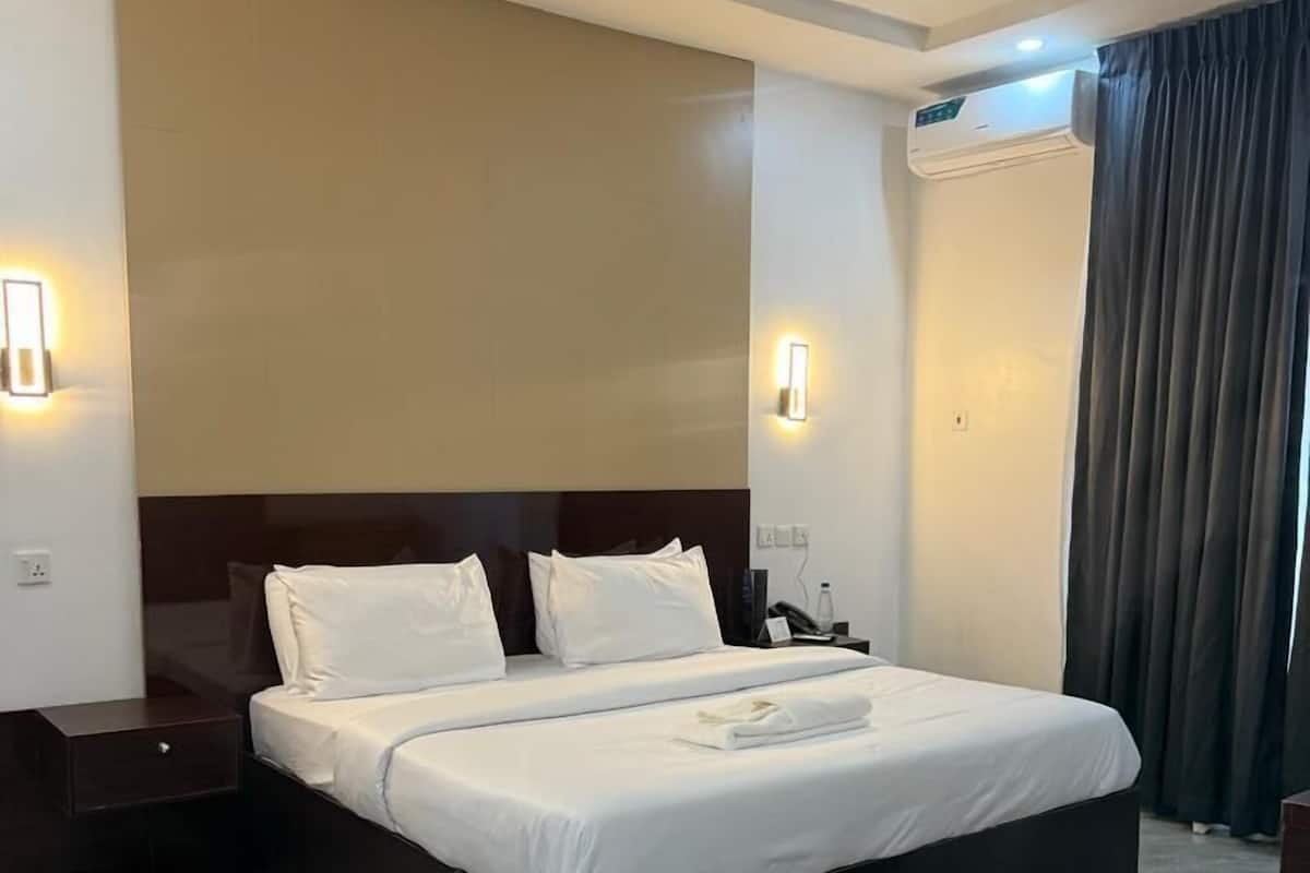 A modern hotel room with a large bed, dark wood headboard, and a marble floor.