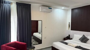 Una camera d'albergo con un letto, una poltrona rossa, un tavolino, uno specchio e un condizionatore d'aria.