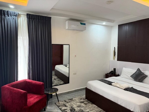 Une chambre d’hôtel avec un lit, un fauteuil rouge, une petite table, un miroir et un appareil de climatisation.