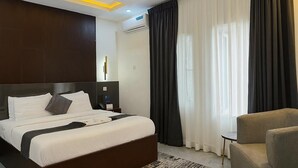 Una camera d'albergo moderna con un letto grande, un comodino, una sedia e una finestra con tende.