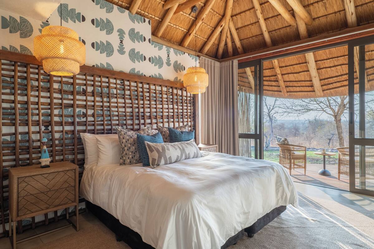 A spacious bedroom with a large bed, wooden headboard, and a view of the outdoors through large windows.