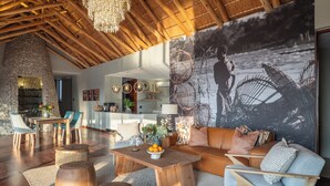 Amplia sala de estar con techo de madera alto, un gran mural en la pared y una entrada con muro de piedra.