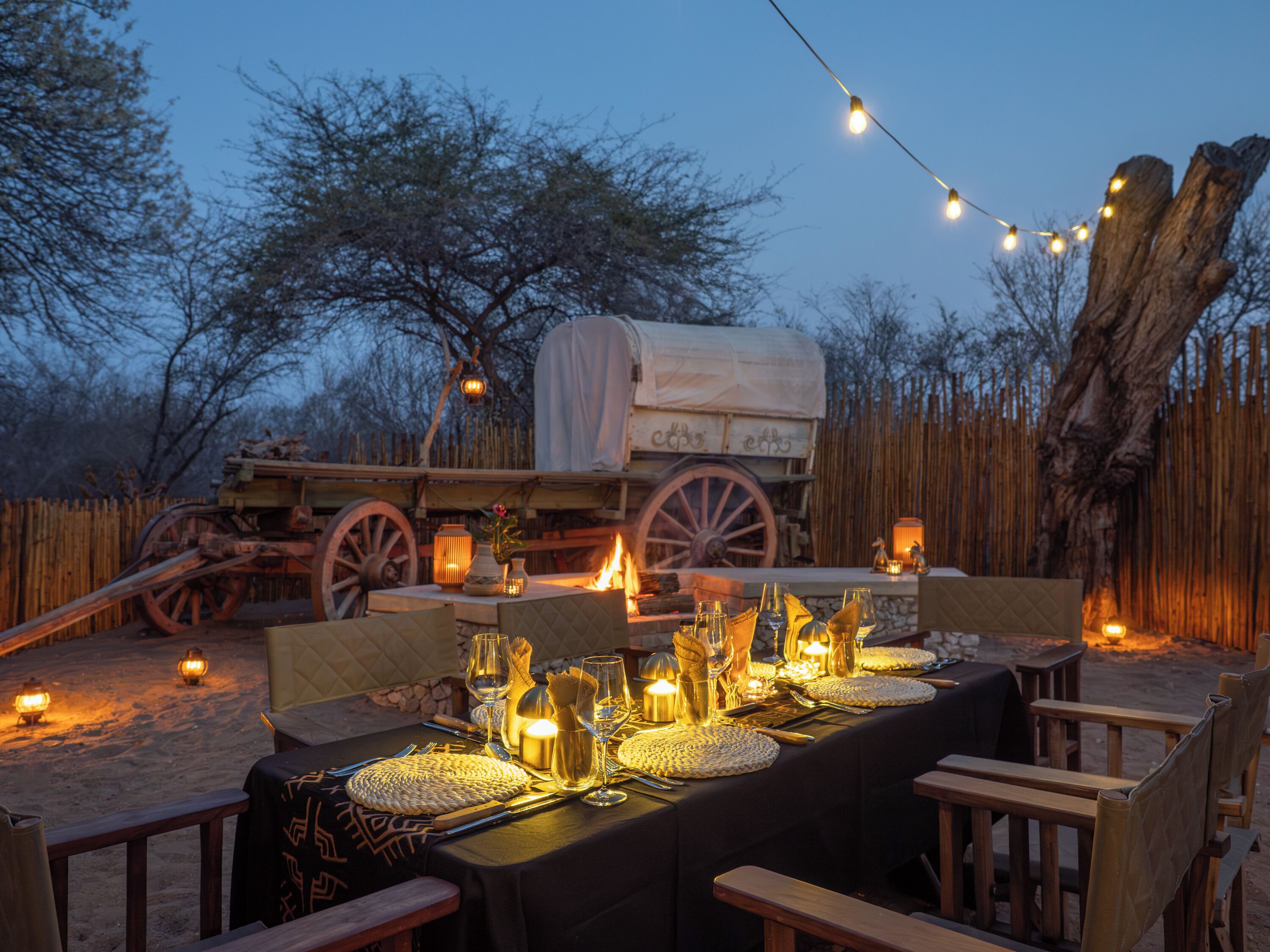 Un área de comedor al aire libre con una mesa cubierta dispuesta para una comida, rodeada de sillas de madera.