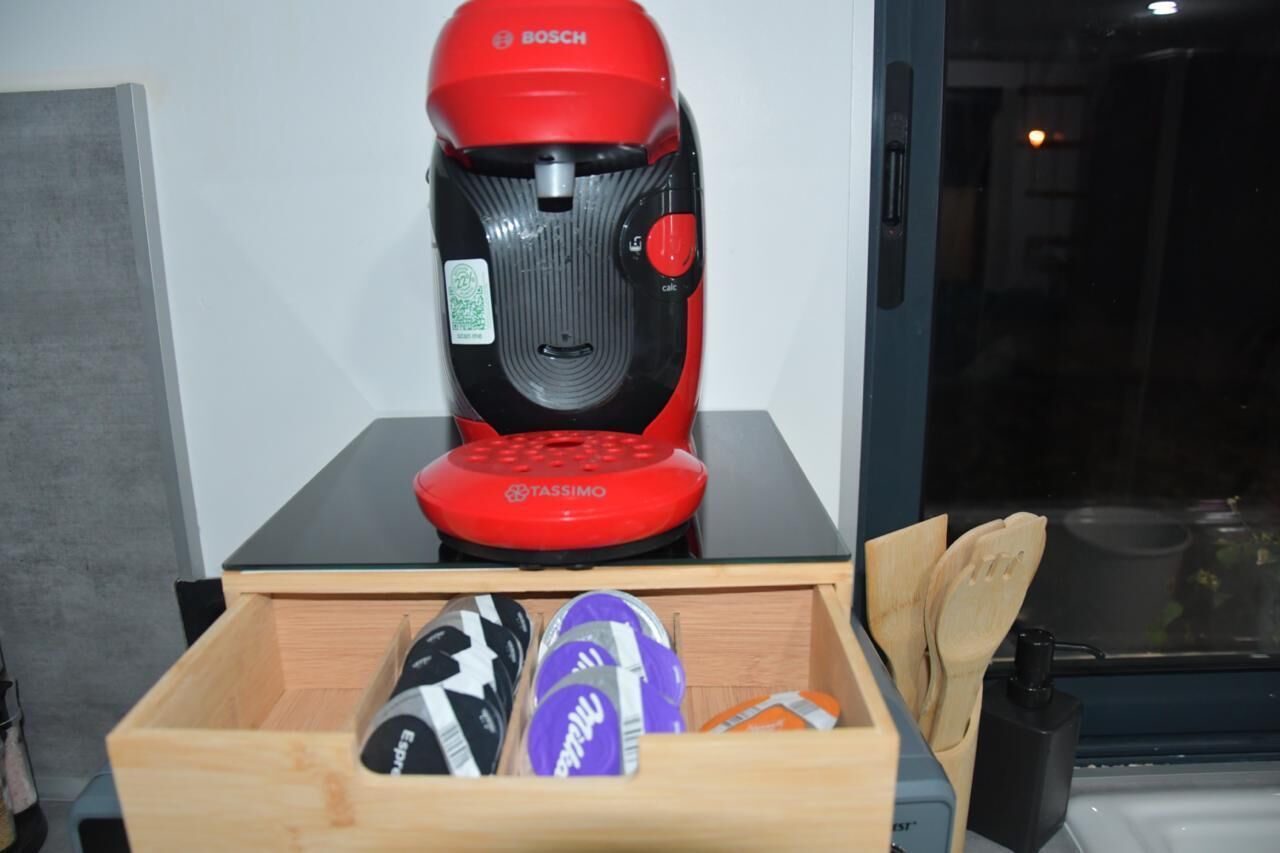 Una cafetera roja Bosch sobre una encimera negra con un cajón de madera debajo que contiene varios objetos.