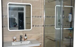 A bathroom with a glass shower enclosure, a sink with two bottles of hand soap, and a mirror.