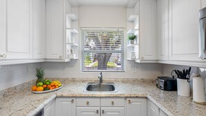A kitchen with white cabinets, a granite countertop, a sink, a toaster, and a fruit bowl. - Bay to Bay Bungalow | Sleeps 6 (Tampa)