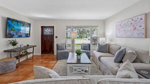 A living room with a sofa, a coffee table, and a TV. There is a door leading to a balcony with a view of the street. - Bay to Bay Bungalow | Sleeps 6 (Tampa)
