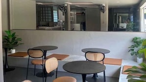 A seating area with round tables and chairs, a large mirror reflecting the room, and potted plants. - Hide Hostel (Koh Phangan)