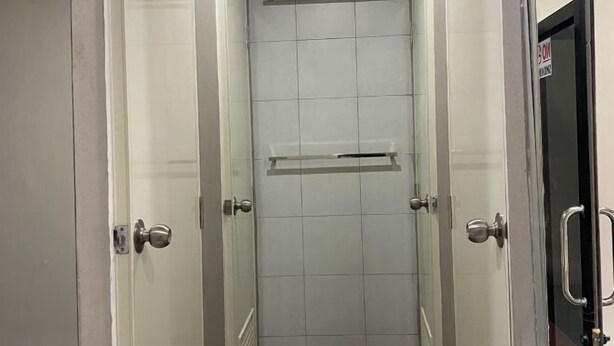 A narrow, tiled shower stall with a horizontal shelf and a door with a handle. - Hide Hostel (Koh Phangan)