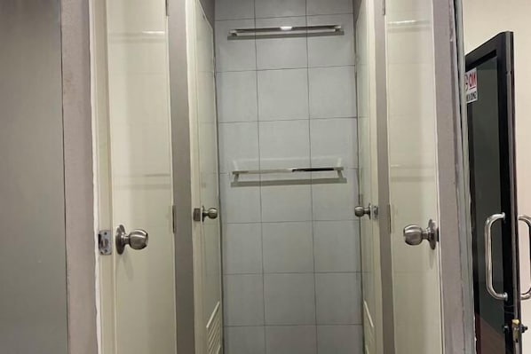 Une petite cabine de douche carrelée, dotée d’une étagère horizontale et d’une porte avec une poignée.