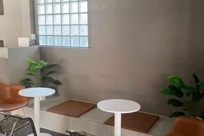 A seating area with two round tables and chairs, a potted plant, and a window with a view. - Hide Hostel (Koh Phangan)