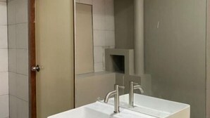 A modern bathroom with a large mirror, a white sink, and a door leading to another room. - Hide Hostel (Koh Phangan)