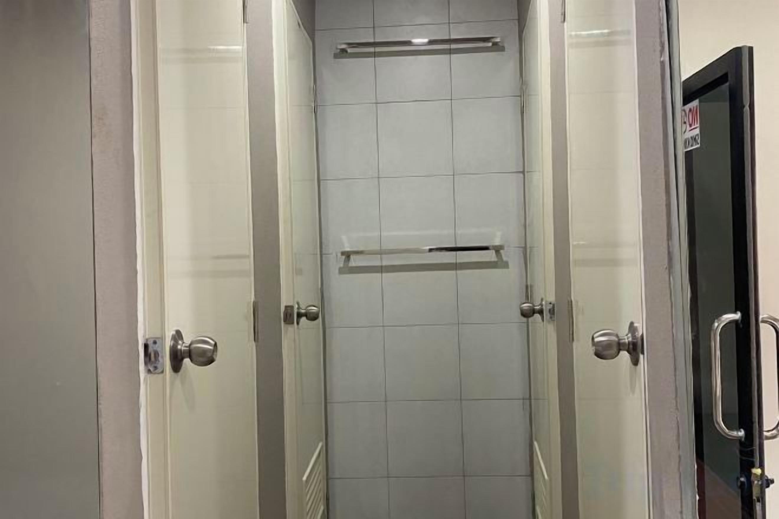 Corredor com portas de vidro que dão para um banheiro com piso ladrilhado e um porta-toalhas.